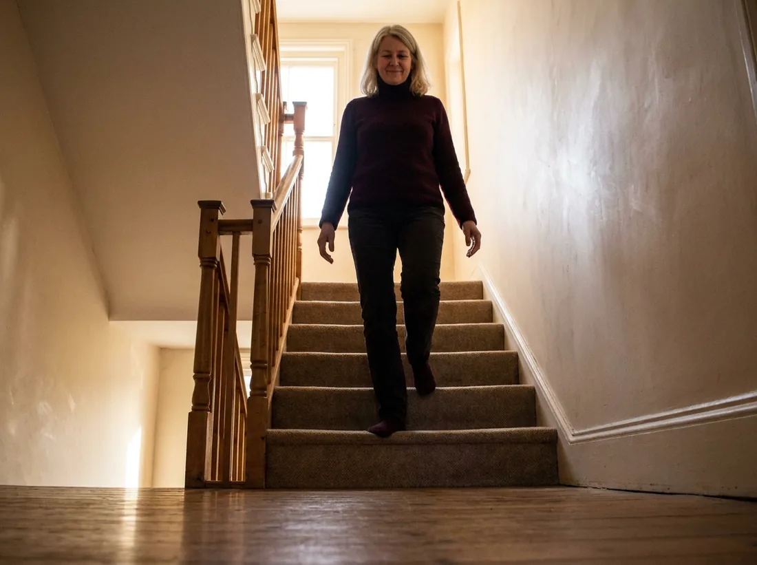 Frau um die fünfzig geht zu Hause die Treppe hinunter, die Hand frei vom Geländer